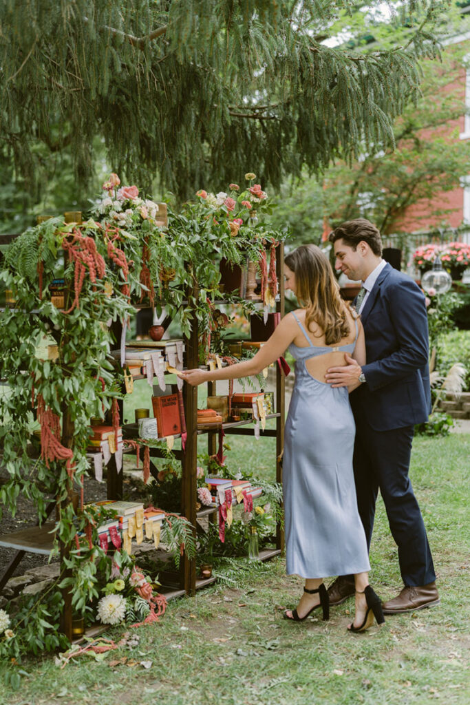 Couple viewing a bookcase escort card display decorated with flowers and greenery