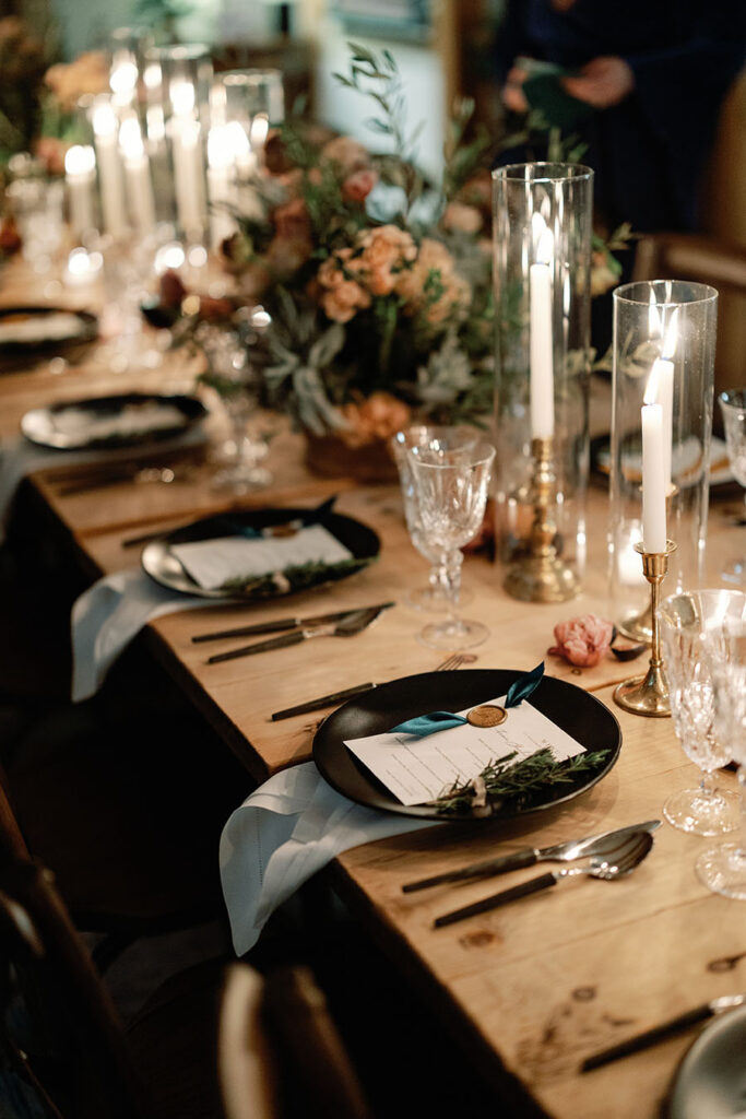 Candlelit Vermont wedding tablescape with dark place settings and seasonal florals
